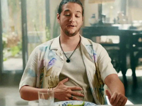 Homem sentado em uma mesa, visivelmente satisfeito, com uma mão sobre o estômago.