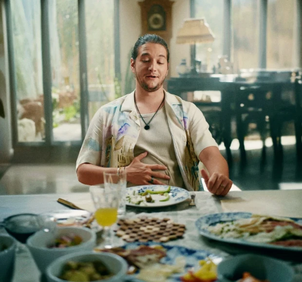 Homem sentado em uma mesa, visivelmente satisfeito, com uma mão sobre o estômago.