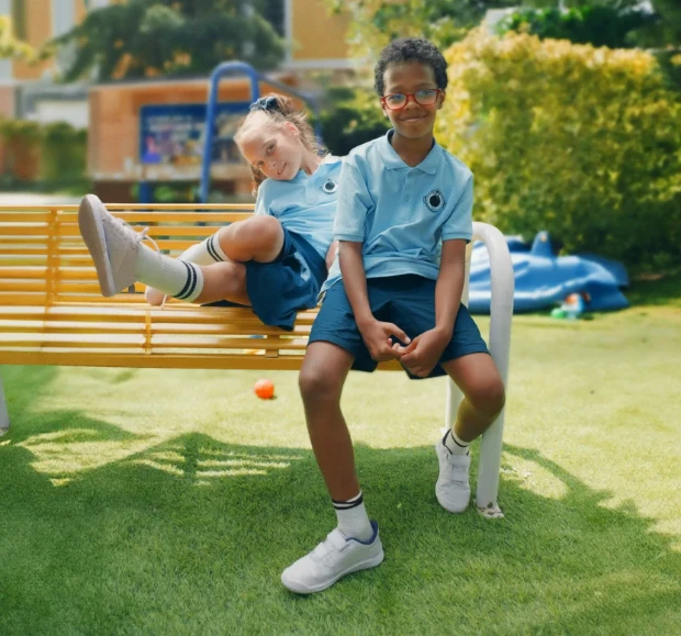 Duas crianças com uniformes azuis combinando, sentadas em um banco de praça.