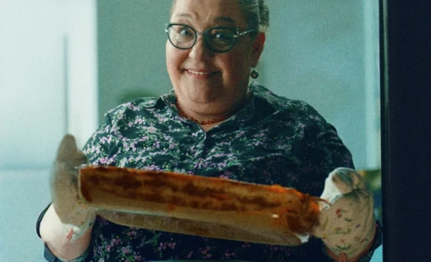 Pessoa sorridente segurando um prato assado com luvas de forno.