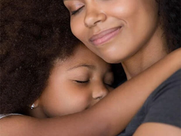 Uma mãe e um filho se abraçam com os olhos fechados, sorrindo com satisfação.