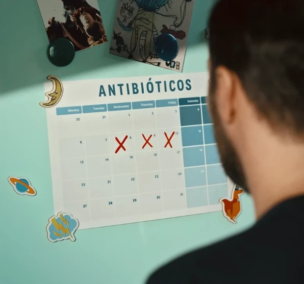 Homem olhando calendário de Antibióticos na geladeira, com dias marcados com 'X