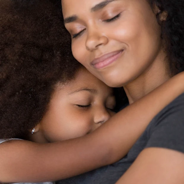 Uma mãe e um filho se abraçam com ternura, ambos com expressões de paz e satisfação.