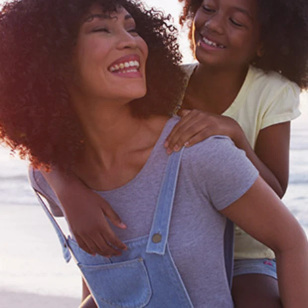 Mulher dando carona a uma criança sorridente na praia.