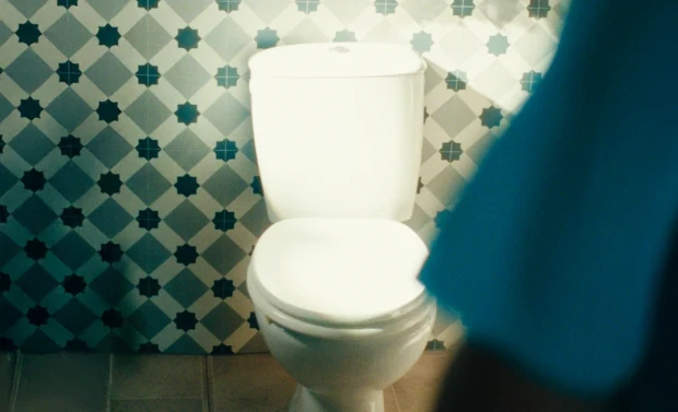 Um vaso sanitário branco contra uma parede de azulejos estampados em um banheiro.