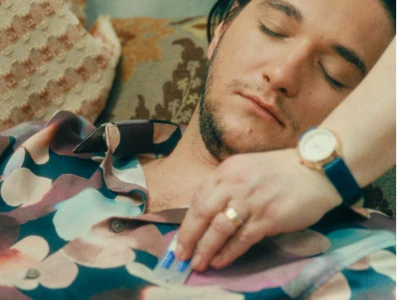 Uma pessoa coloca uma embalagem blister azul no bolso da camisa de um homem que está dormindo.