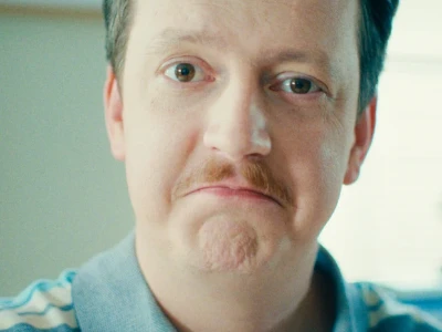 Homem de bigode vestindo uma camisa de colarinho azul-claro.