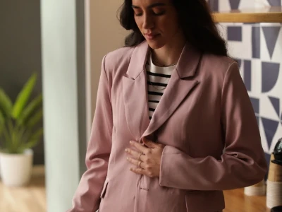 Pessoa em um blazer rosa olhando para baixo com a mão no estômago.