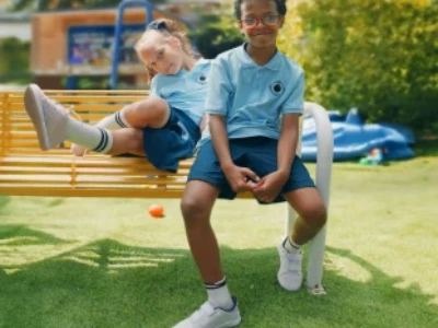 Duas crianças com uniformes azuis sentadas em um banco do playground.