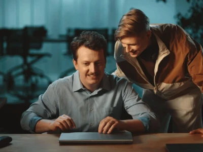 Duas pessoas sorrindo para um laptop fechado em uma mesa.