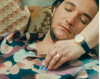 Uma pessoa coloca uma embalagem blister azul no bolso da camisa de um homem que está dormindo.