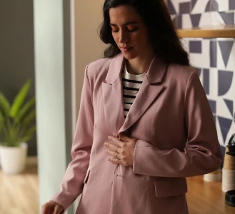 Pessoa em um blazer rosa olhando para baixo com a mão no estômago.