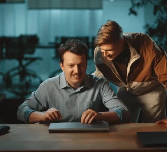 Duas pessoas sorrindo para um laptop fechado em uma mesa.
