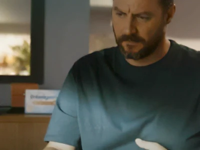 Um homem em uma sala mal iluminada segura seu estômago, parecendo desconfortável.