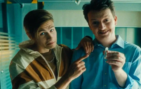 Duas pessoas sorrindo, uma delas segurando um pequeno objeto.