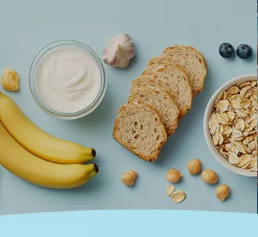 Bananas, iogurte, alho, pão, aveia, mirtilos e grão de bico em um fundo azul.