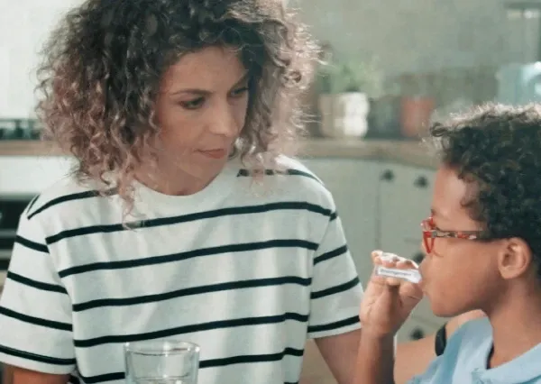 Mulher observando criança tomando Enterogermina suspensão oral em uma cozinha.