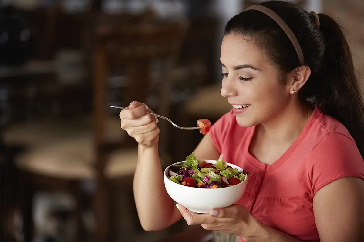 Mujer disfrutando de una ensalada fresca y nutritiva, contribuyendo a mejorar su salud intestinal y normalizar la producción de heces.