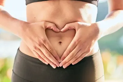Mãos formando um coração na barriga nua de uma mulher.