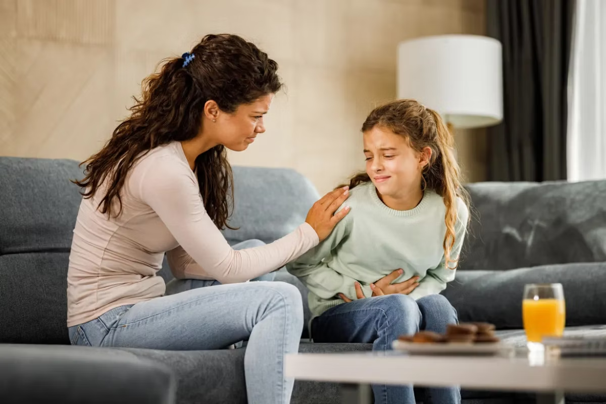 Una niña que se queja de dolor de estómago a su madre, recordándonos la importancia de la salud digestiva en la vida familiar.