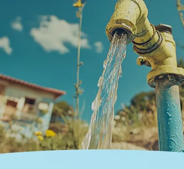 Água fluindo de uma torneira externa com uma casa e grama ao fundo.