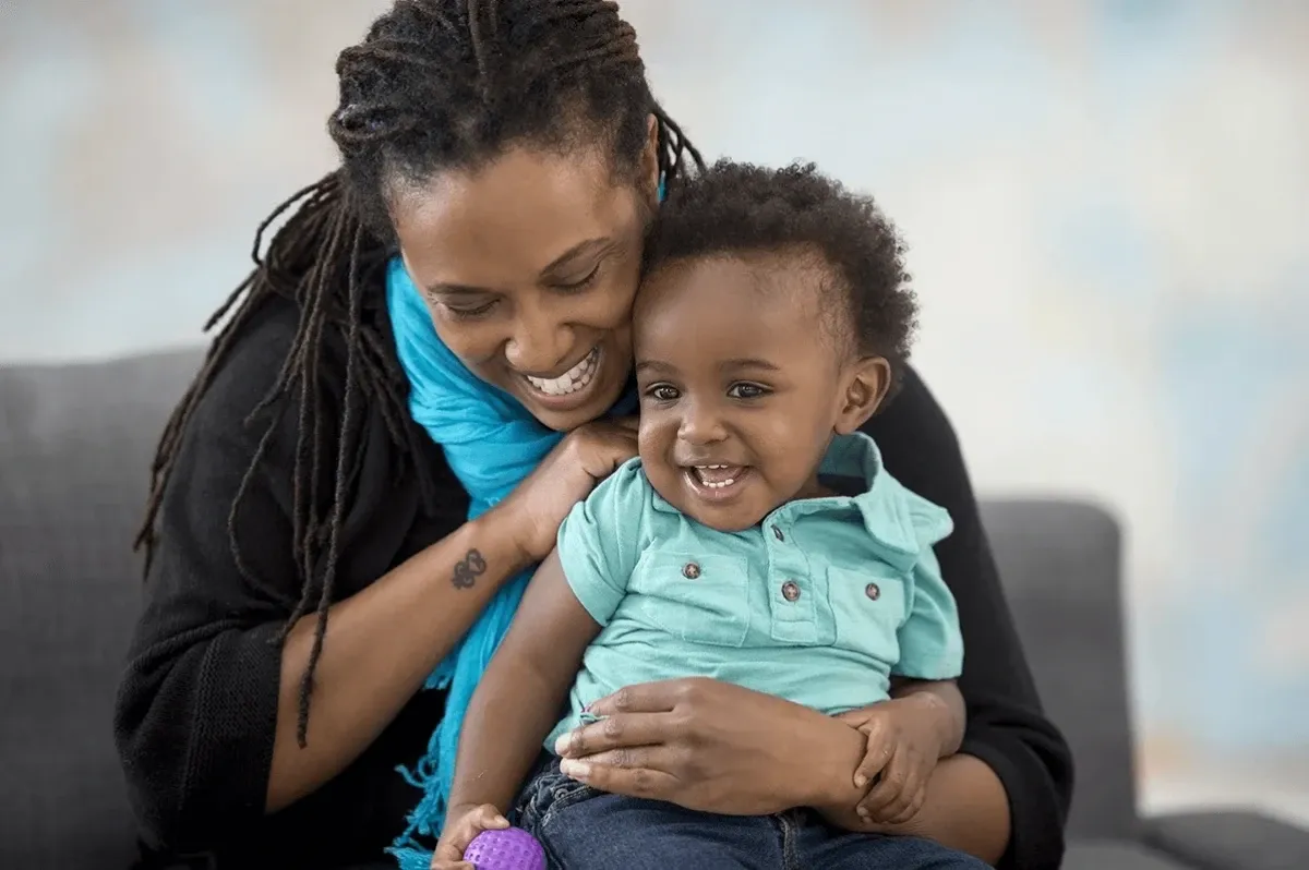 Uma mulher de aparência carinhosa está sorrindo para o bebê em seu colo, que está segurando uma bola.