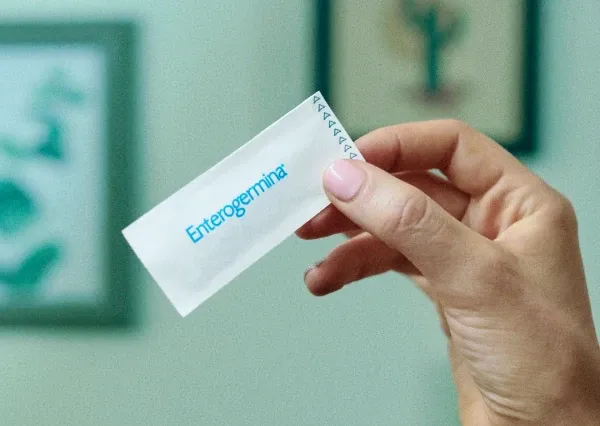 Mão segurando uma embalagem de sachê probiótico Enterogermina.