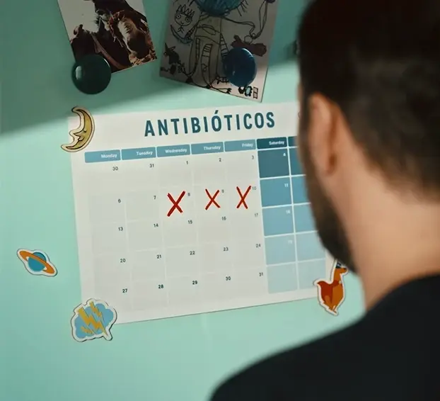 Homem olhando para um calendário intitulado "Antibióticos" com três dias marcados com Xs vermelhos.
