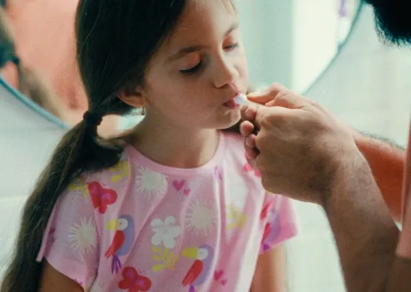 Criança com camisa rosa tomando remédio em um conta-gotas.