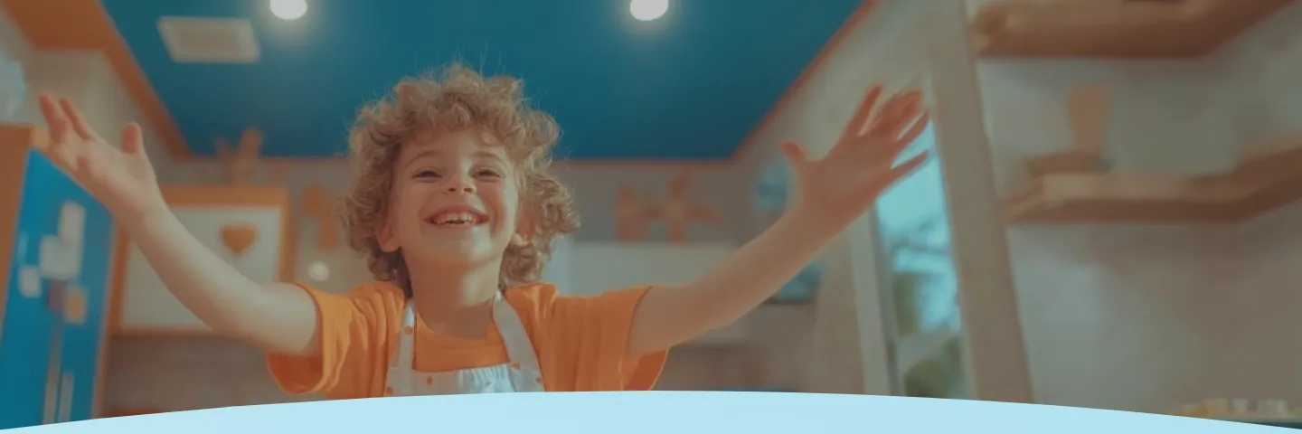 Criança com cabelo cacheado sorrindo e usando um avental em uma cozinha colorida.