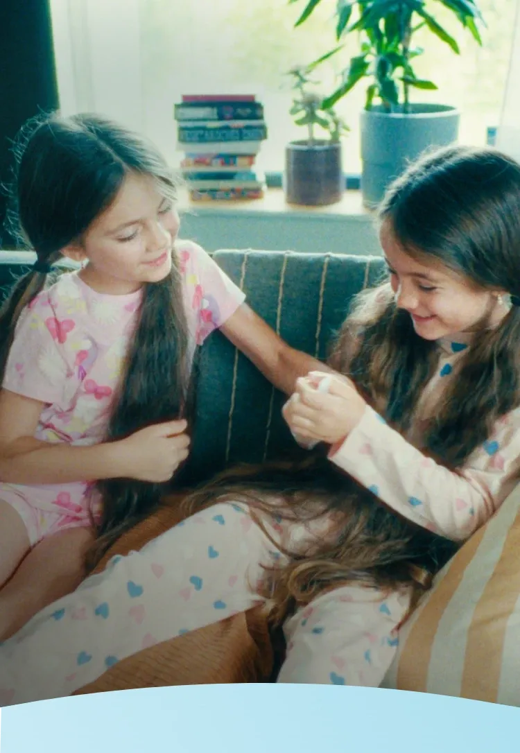 Duas jovens de pijama sentadas em um sofá, sorrindo e brincando com os cabelos.