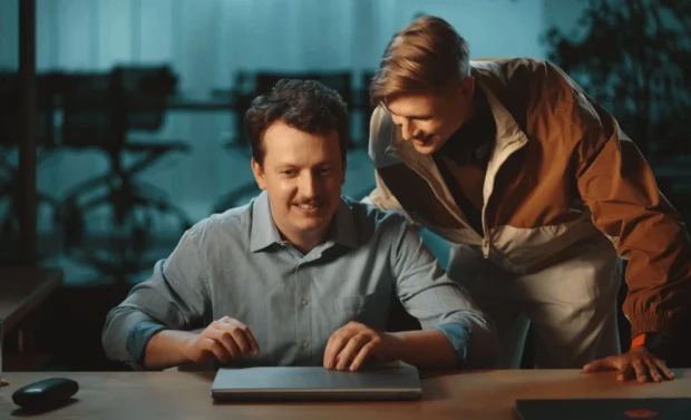 Duas pessoas sorrindo para um laptop fechado em um ambiente de escritório.