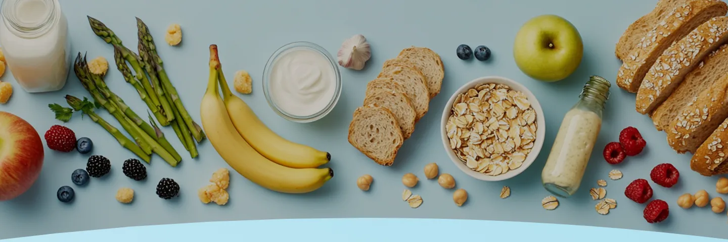 Vários alimentos, incluindo frutas, pão, iogurte e aspargos, dispostos em uma superfície azul-clara.