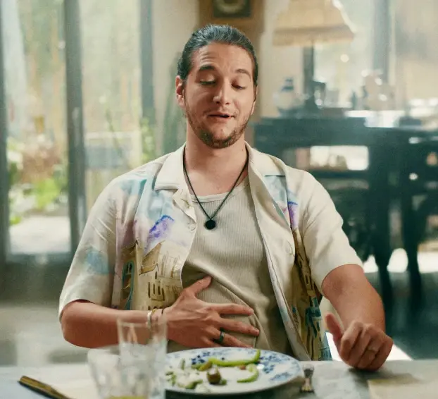 Homem sentado em uma mesa, visivelmente satisfeito, com uma mão sobre o estômago.