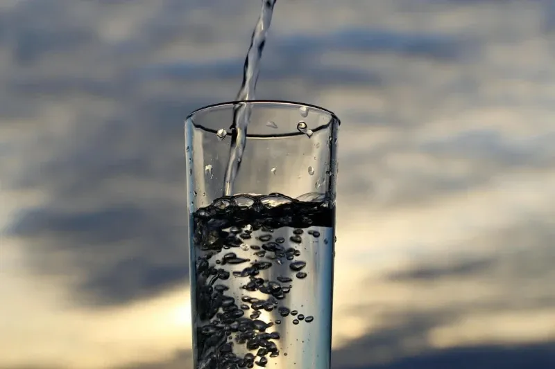 Água sendo despejada em um copo com um fundo de céu nublado.