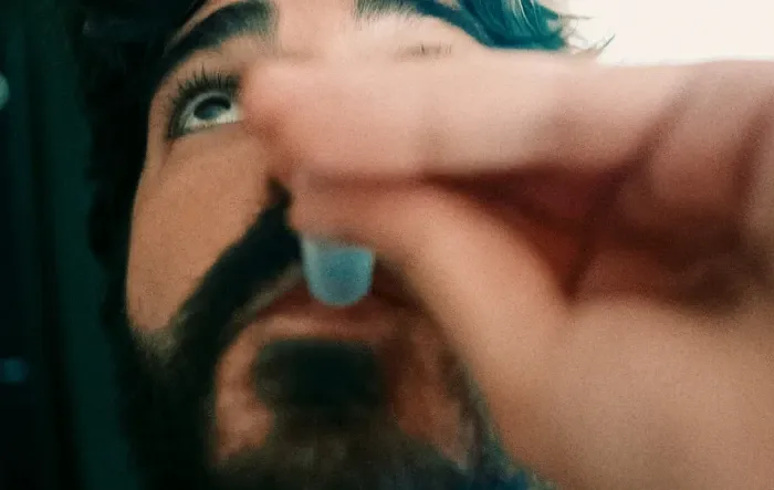 Uma pessoa segurando um pequeno frasco próximo à boca.