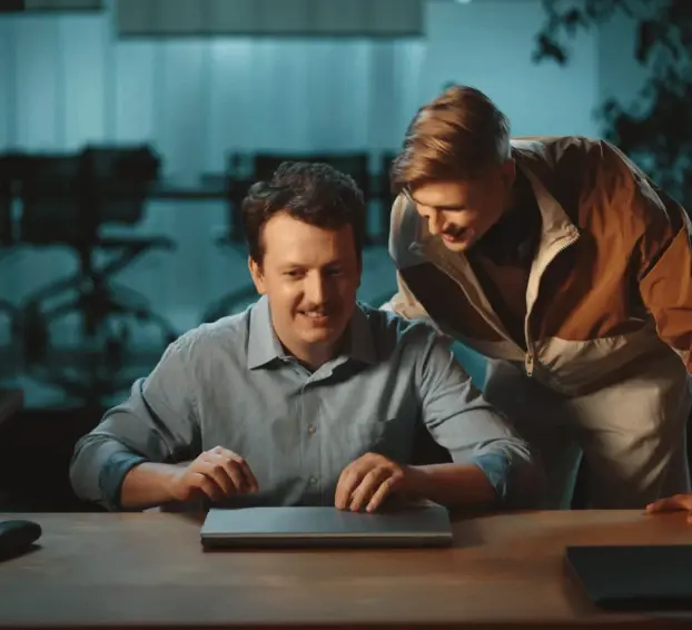 Duas pessoas sorrindo para um laptop fechado em uma mesa.