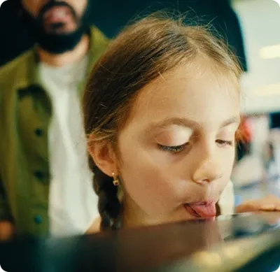 Criança com tranças encostando a língua em uma superfície de vidro.