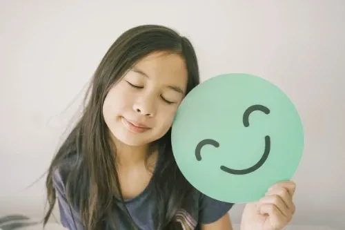 uma criança segurando um emogi impresso com sembrante feliz