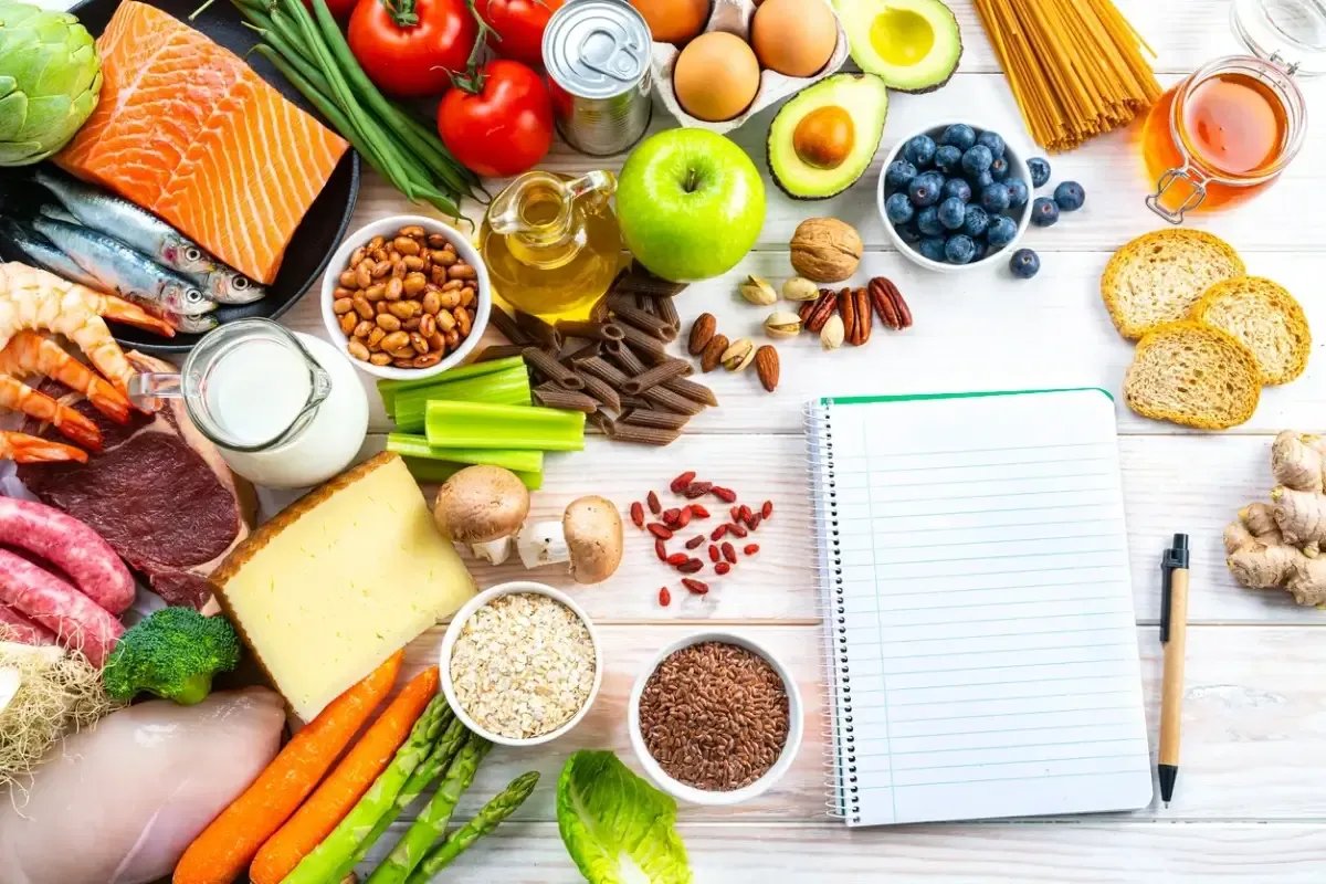 diversos alimentos ricos em fibras em cima de uma mesa vistos de cima com um caderno ao lado