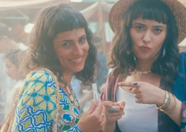 Duas mulheres sorrindo e apontando para um produto em um ambiente externo animado.