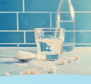 Copo de água com açúcar, colher e garrafa em um balcão de cozinha com fundo de azulejo azul.