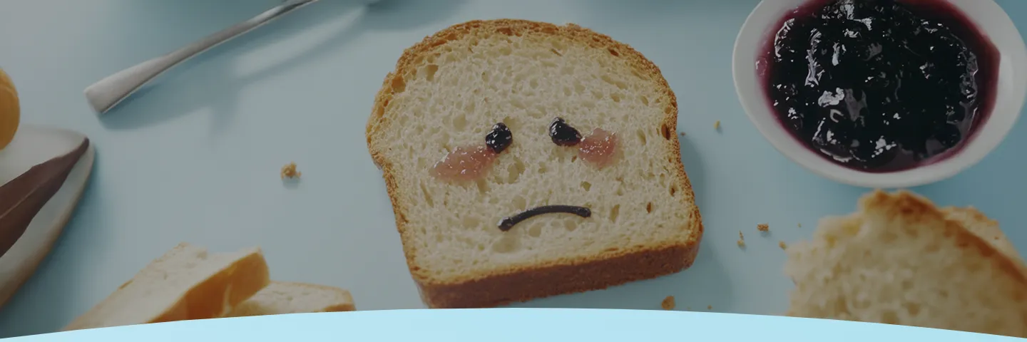 Fatia de pão com uma cara triste feita de geleia ao lado de uma tigela com mais geleia e migalhas de torrada.