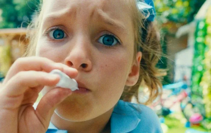 Uma criança concentrada com olhos azuis bebe de uma pequena garrafa ao ar livre.
