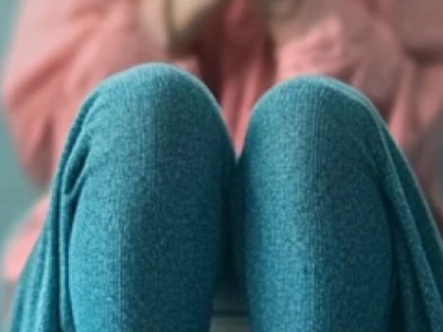 Pessoa sentada com os joelhos para cima, vestindo calça azul-petróleo e blusa rosa.