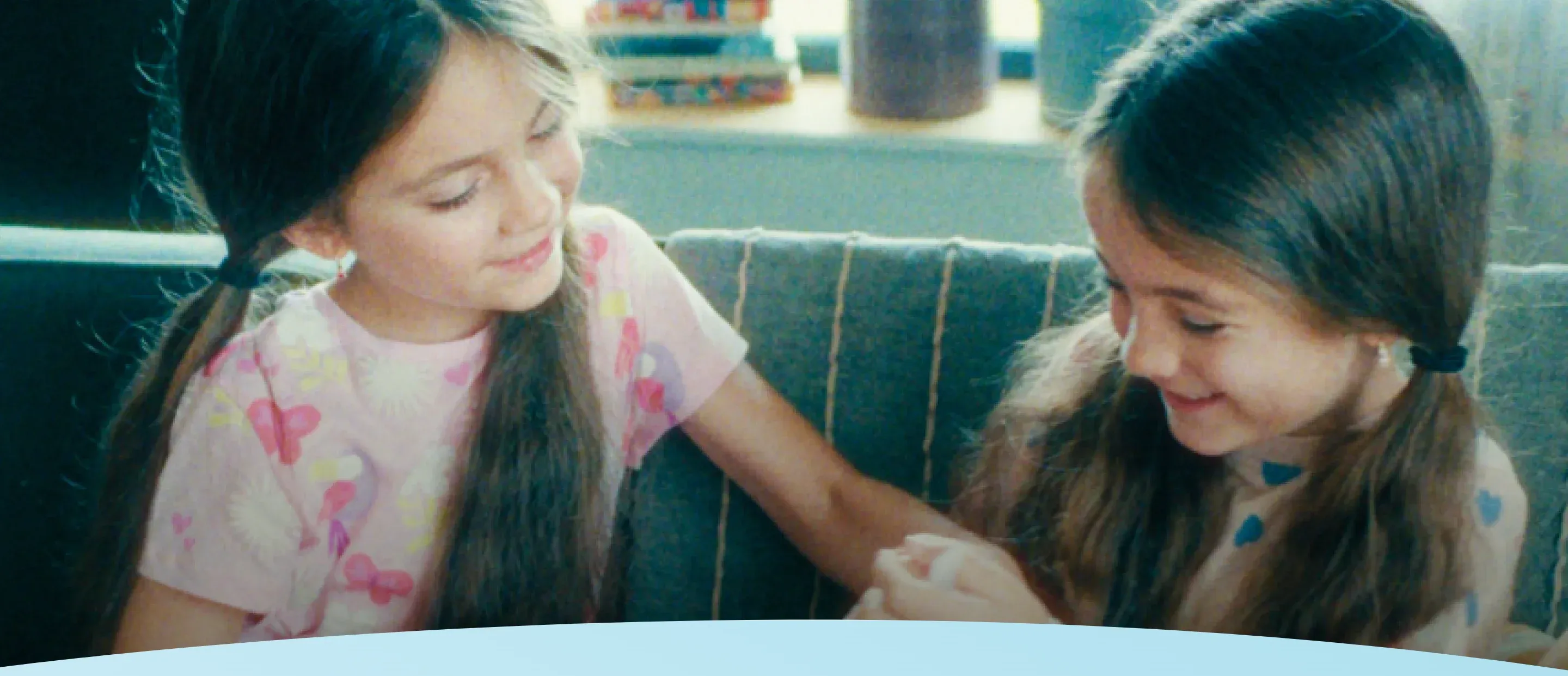 Duas crianças sentadas em um sofá, sorrindo e olhando para suas mãos.