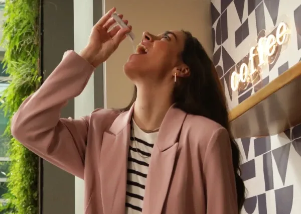 Pessoa de blazer rosa tomando um suplemento líquido em uma cafeteria.