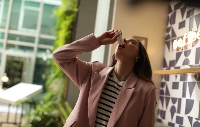 Mulher tomando probiótico Enterogermina de um flaconete em cafeteria
