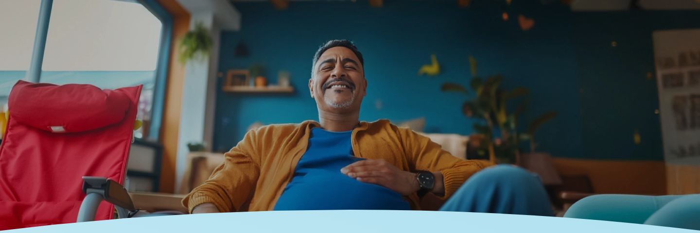 Um homem relaxado sorri satisfeito, sentado em um ambiente interno e aconchegante.