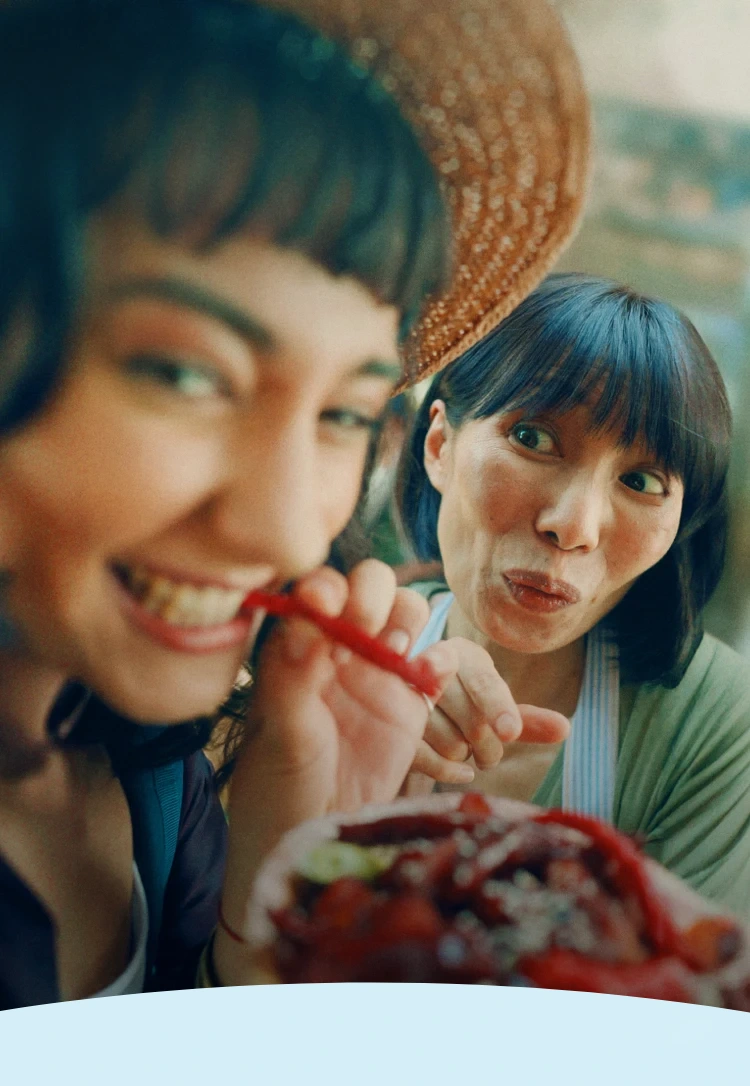 Duas mulheres sorrindo e comendo pimentas vermelhas com expressão divertida.